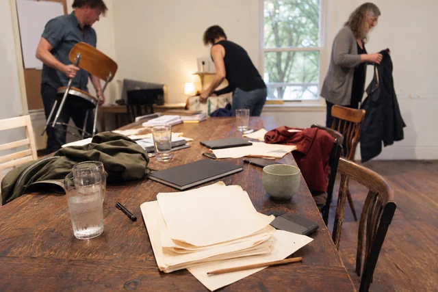Writers pack up around a table scattered with manuscripts after a session