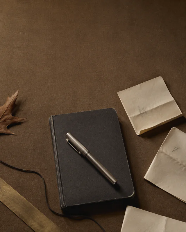 A black notebook and steel pen surrounded by folded notes on a brown table