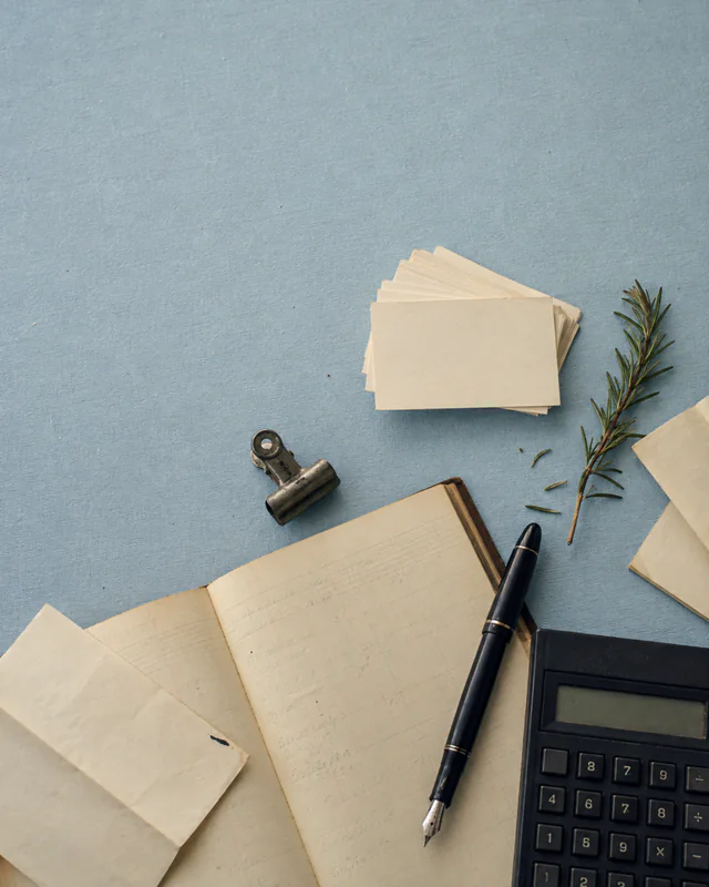 A ledger, calculator, pen, receipts, and clipped notes on a blue table