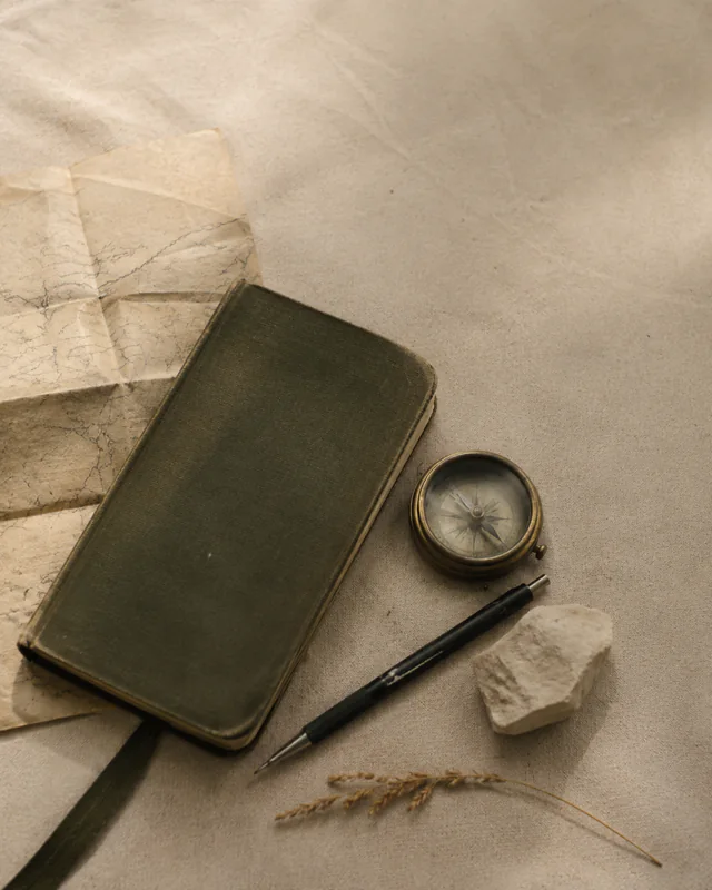 A field notebook, compass, map, and pen arranged for a journey