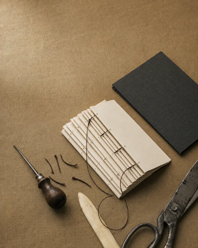 A hand-bound journal with bookbinding tools, thread, scissors, and a dark cover