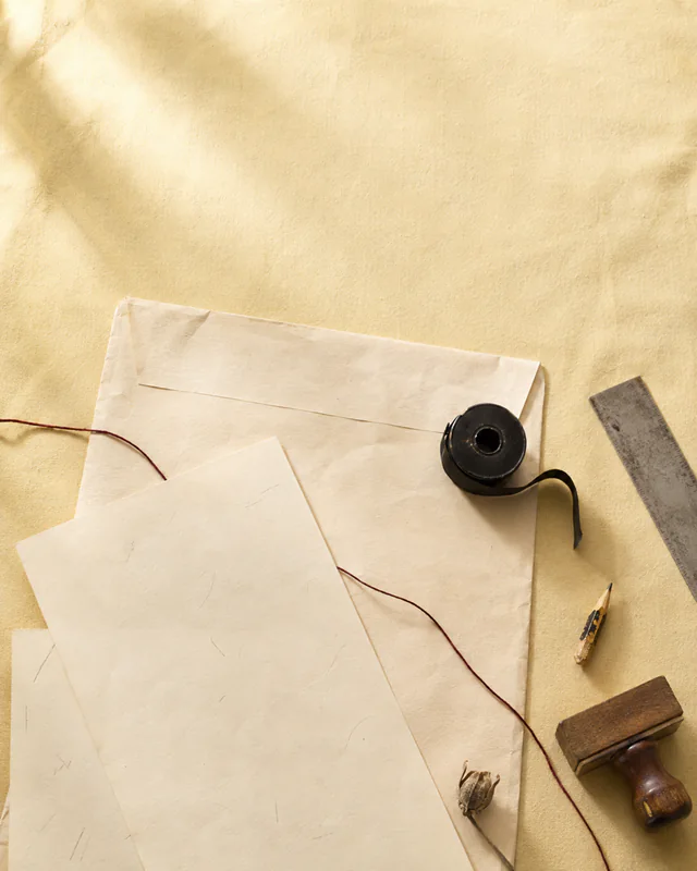 Submission pages, red thread, an ink bottle, ruler, and stamp in warm sunlight