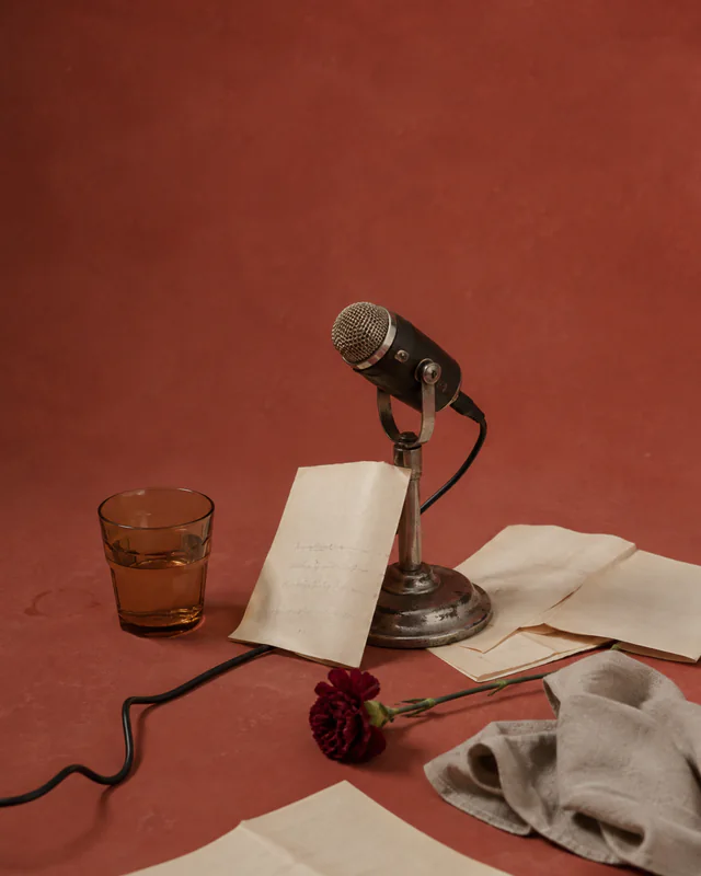 A vintage microphone, reading pages, red flower, and glass on a red stage