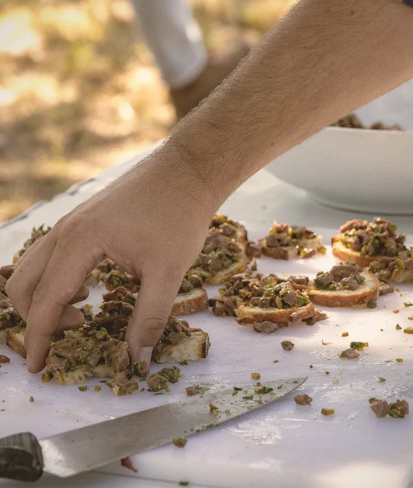 A hand arranges freshly prepared food on slices of bread outdoors