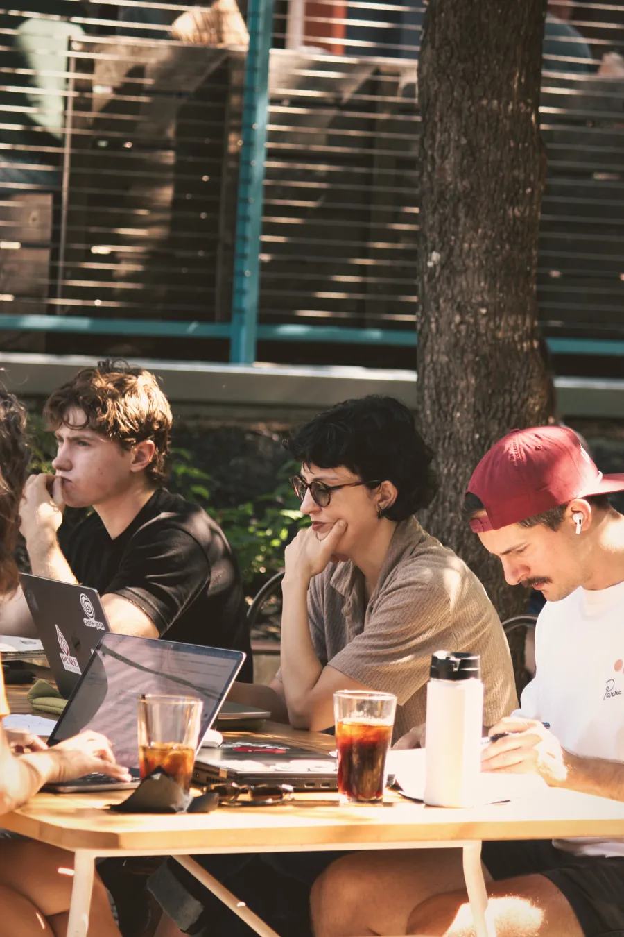 Writers working around an outdoor table with notebooks, laptops, and drinks