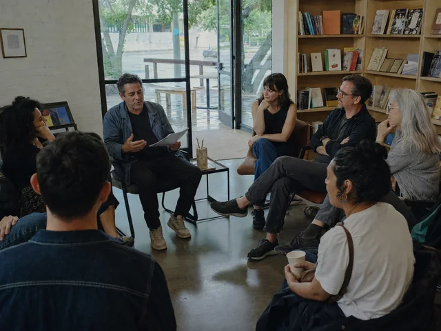 An author reads from a page while writers listen in a circle
