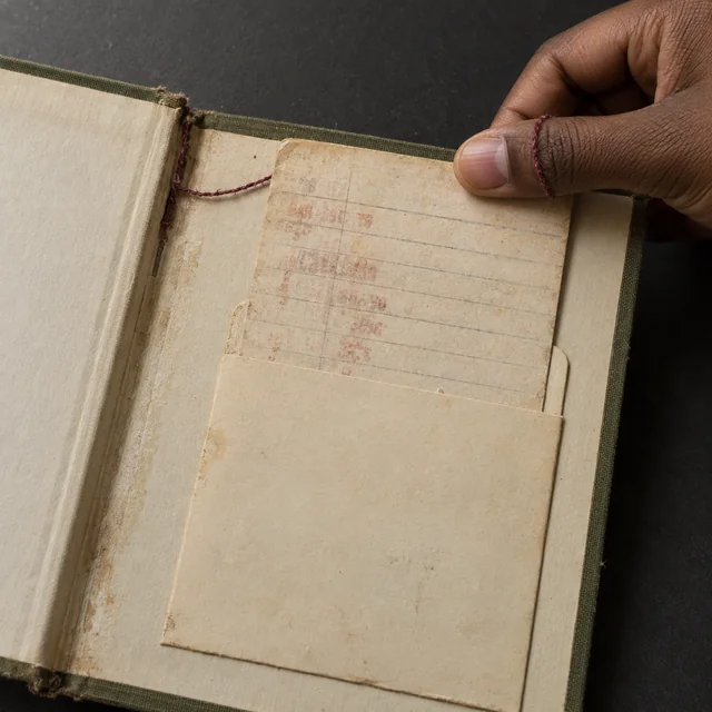 A hand opens a well-used library book to an empty paper pocket