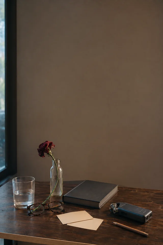 A book, audio recorder, blank note cards, water, and a single flower wait on a speaker table