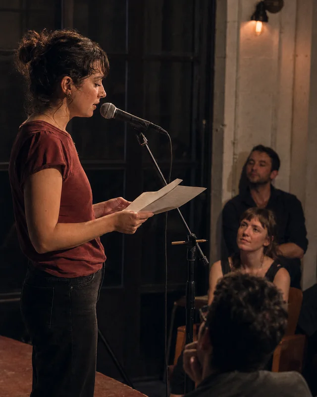 A writer reads from printed pages at a microphone before a seated audience